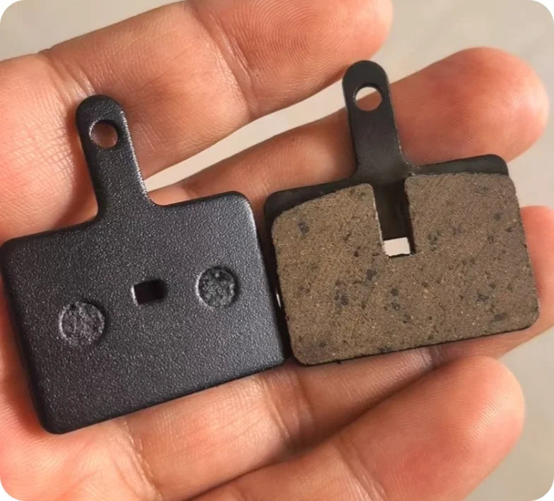 Deux plaquettes de frein résine noires tenues dans la main