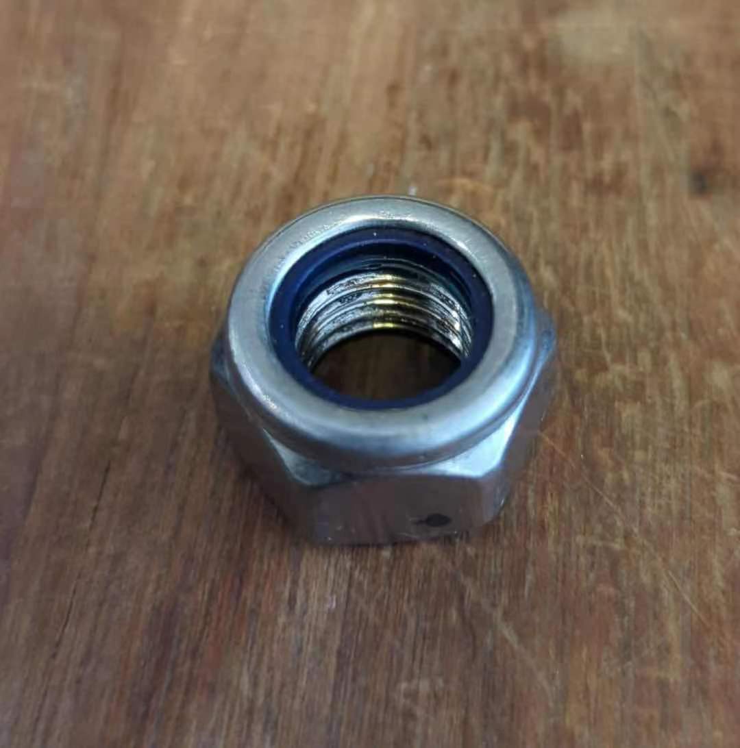 Écrou frein M12 métallisé avec bague interne en nylon bleu posé sur un fond en bois