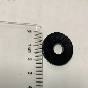 Rondelle noire de 8x25x2 mm posée à côté d'une règle de mesure graduée
