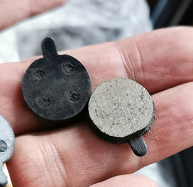 Paire de plaquettes de frein rondes Jak pour trottinette électrique tenues dans une main