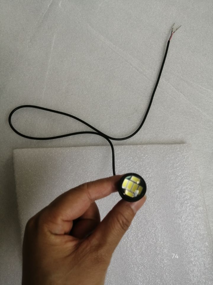 Feu avant rond à LED blanche avec son câble d'alimentation tenu à la main